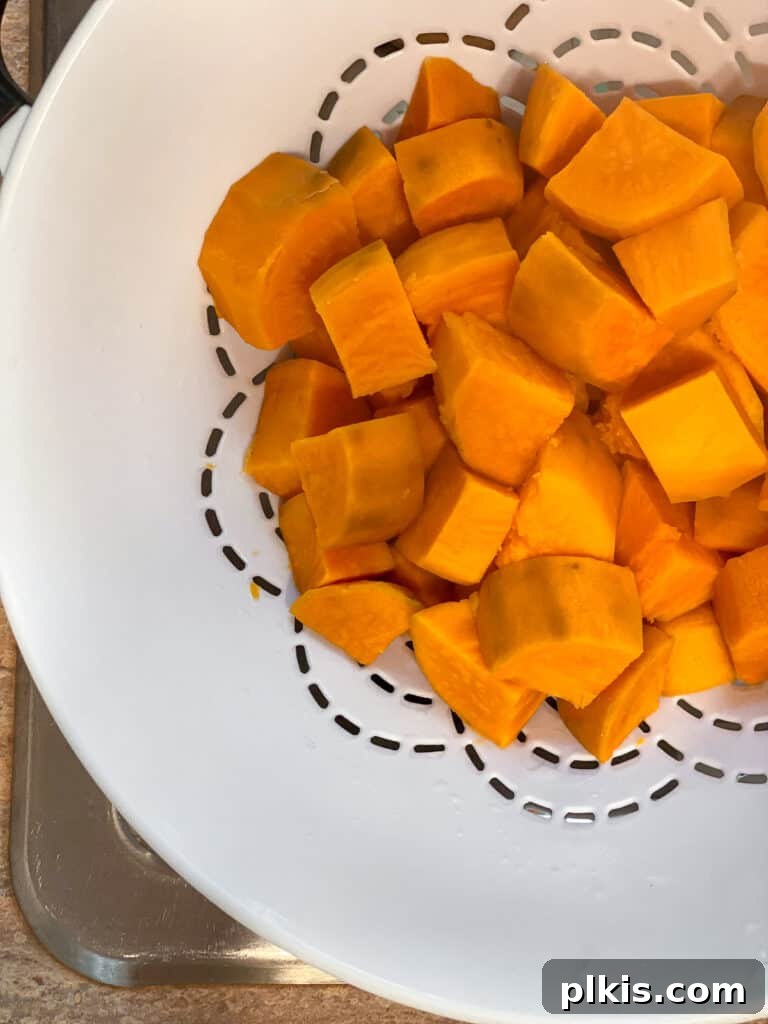 Creamy Vegan Sweet Potato Dream 6 Cooked, cubed sweet potatoes being drained in a metal strainer after boiling.