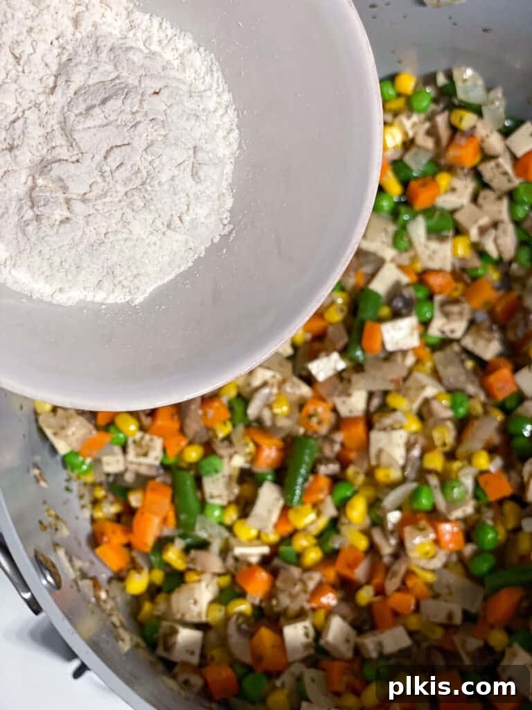 A sprinkle of all-purpose flour is added to the vegetable mixture in the pan, a crucial step for thickening the creamy pot pie sauce.