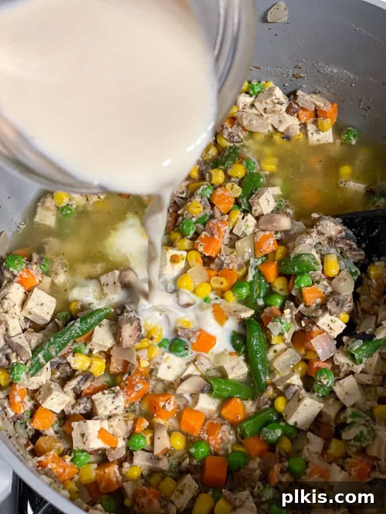Plant-based milk is being added to the simmering vegetable and broth mixture, further enriching and thickening the creamy sauce for the vegan pot pie.
