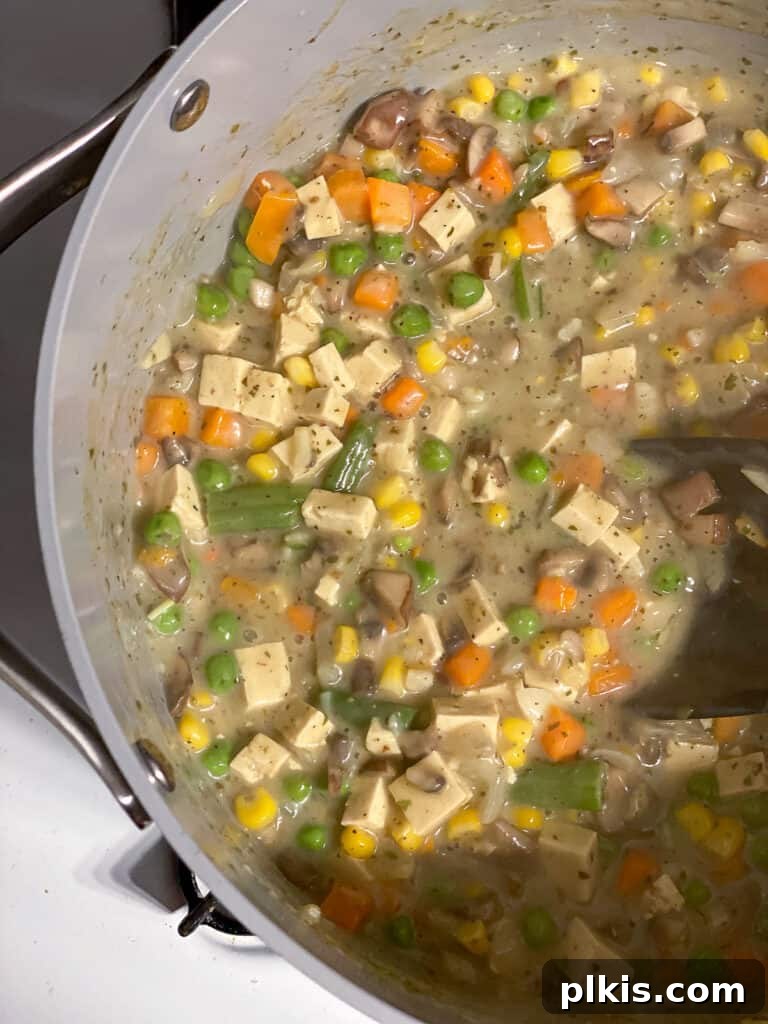 The creamy, rich sauce for the vegan pot pie, featuring mixed vegetables and tofu, is simmering in the pan, perfectly thickened and ready for assembly.