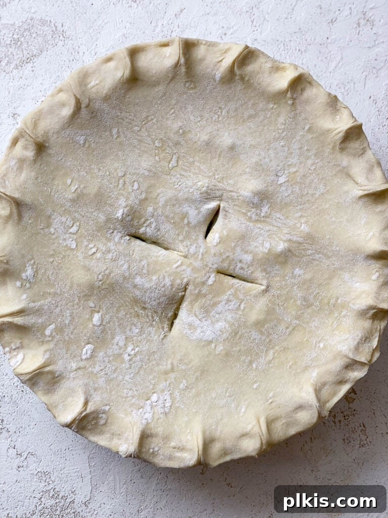 An unbaked Mixed Vegetable Vegan Pot Pie, assembled with a golden puff pastry top crust and steam vents, resting on a white surface, ready for the oven.