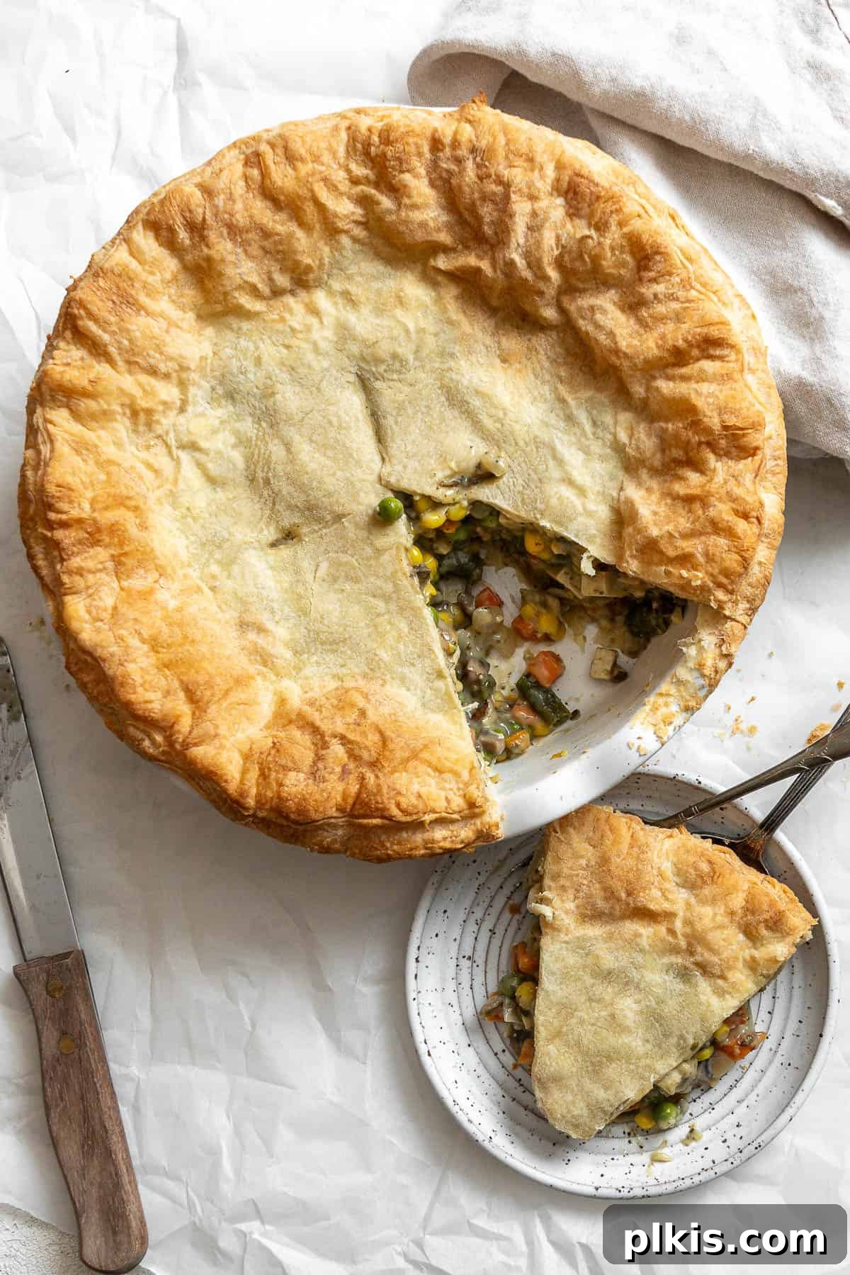 A freshly baked Mixed Vegetable Vegan Pot Pie, golden brown and flaky, rests beautifully on a white surface, steam gently rising, ready to be served.