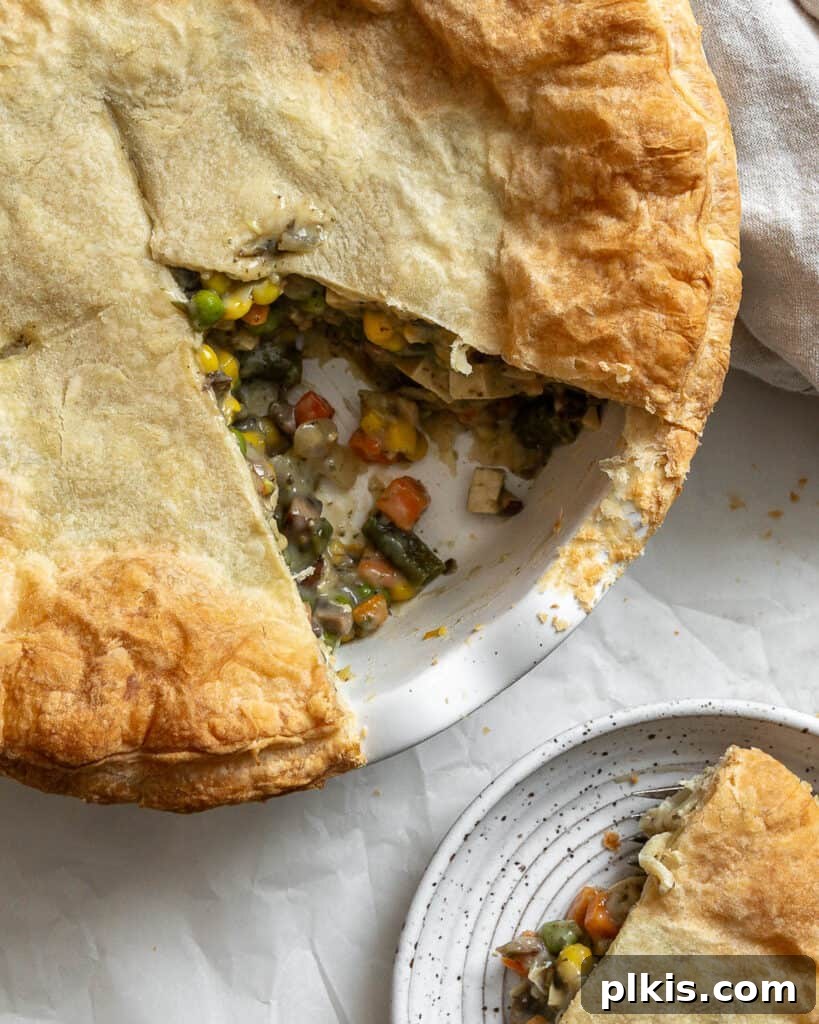 A slice of golden, flaky Mixed Vegetable Vegan Pot Pie, showing the rich, creamy filling, served on a white plate, ready to be enjoyed.