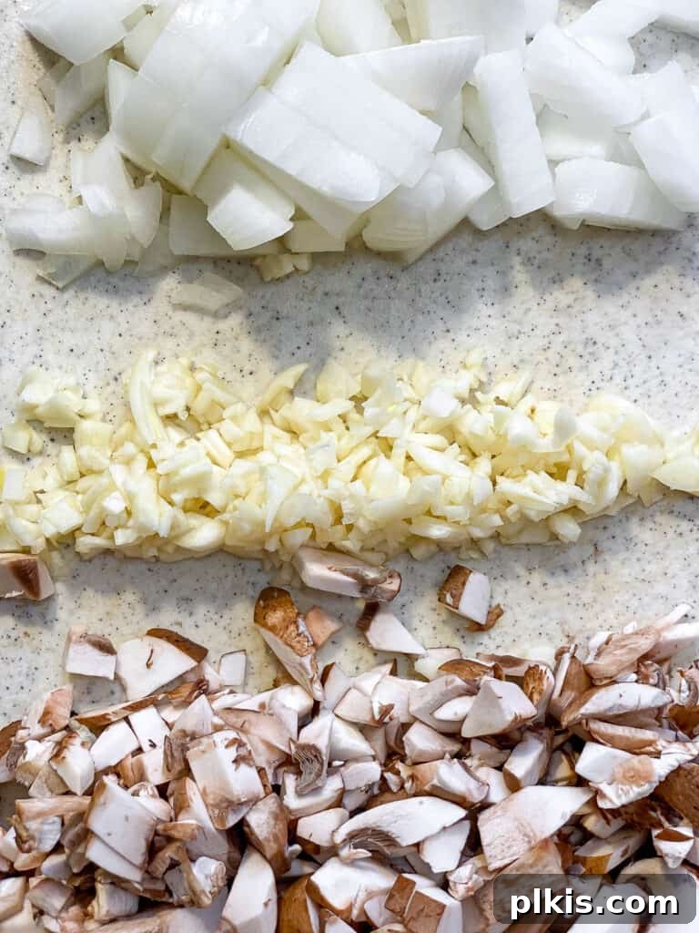 Diced onions, minced garlic, chopped mushrooms, and cubed tofu, all prepped and ready for the vegan pot pie filling, arranged on a cutting board.