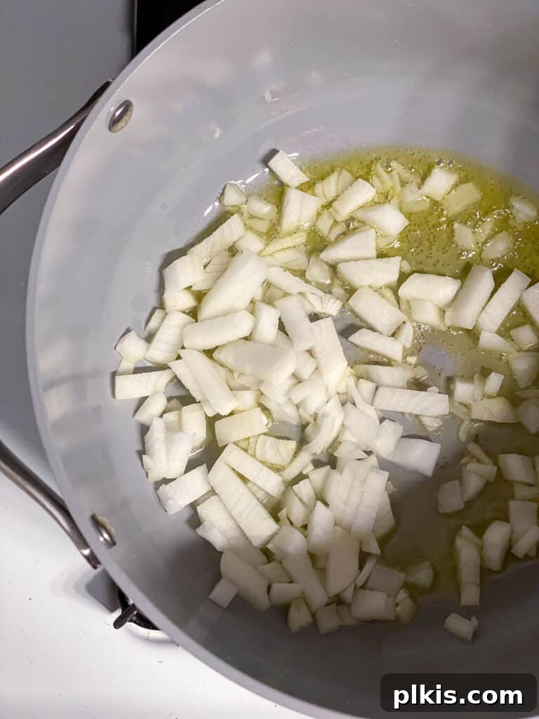 Diced onions sizzling in olive oil in a large skillet, beginning to soften and turn translucent, forming the aromatic base of the pot pie filling.