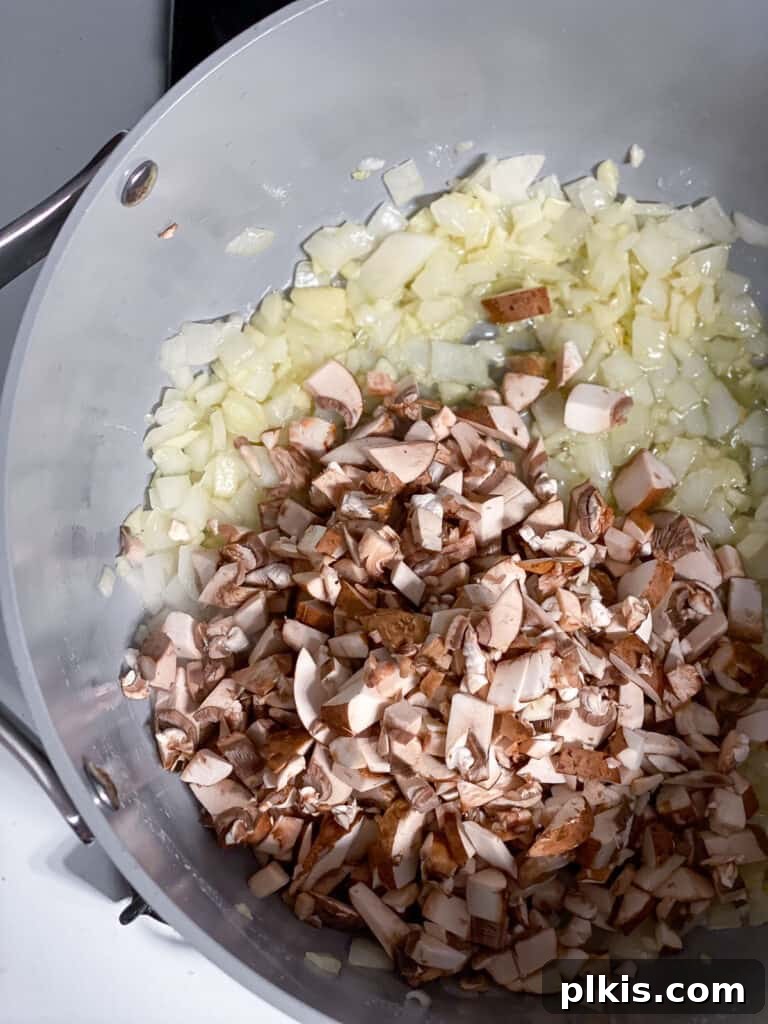 Sliced mushrooms added to the skillet with sautéed onions and garlic, beginning to cook down and integrate into the aromatic base for the pot pie filling.