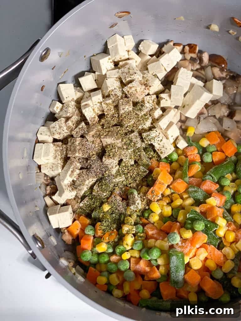 Cubed tofu is added to the pan containing mixed vegetables and aromatics, ready to be incorporated into the savory filling for the vegan pot pie.