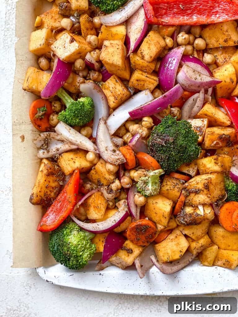 Harvest Roasted Pumpkin Couscous Salad 5 Seasoned mixed vegetables, including pumpkin, chickpeas, and broccoli, spread evenly on a baking tray lined with parchment paper, prepared for roasting.