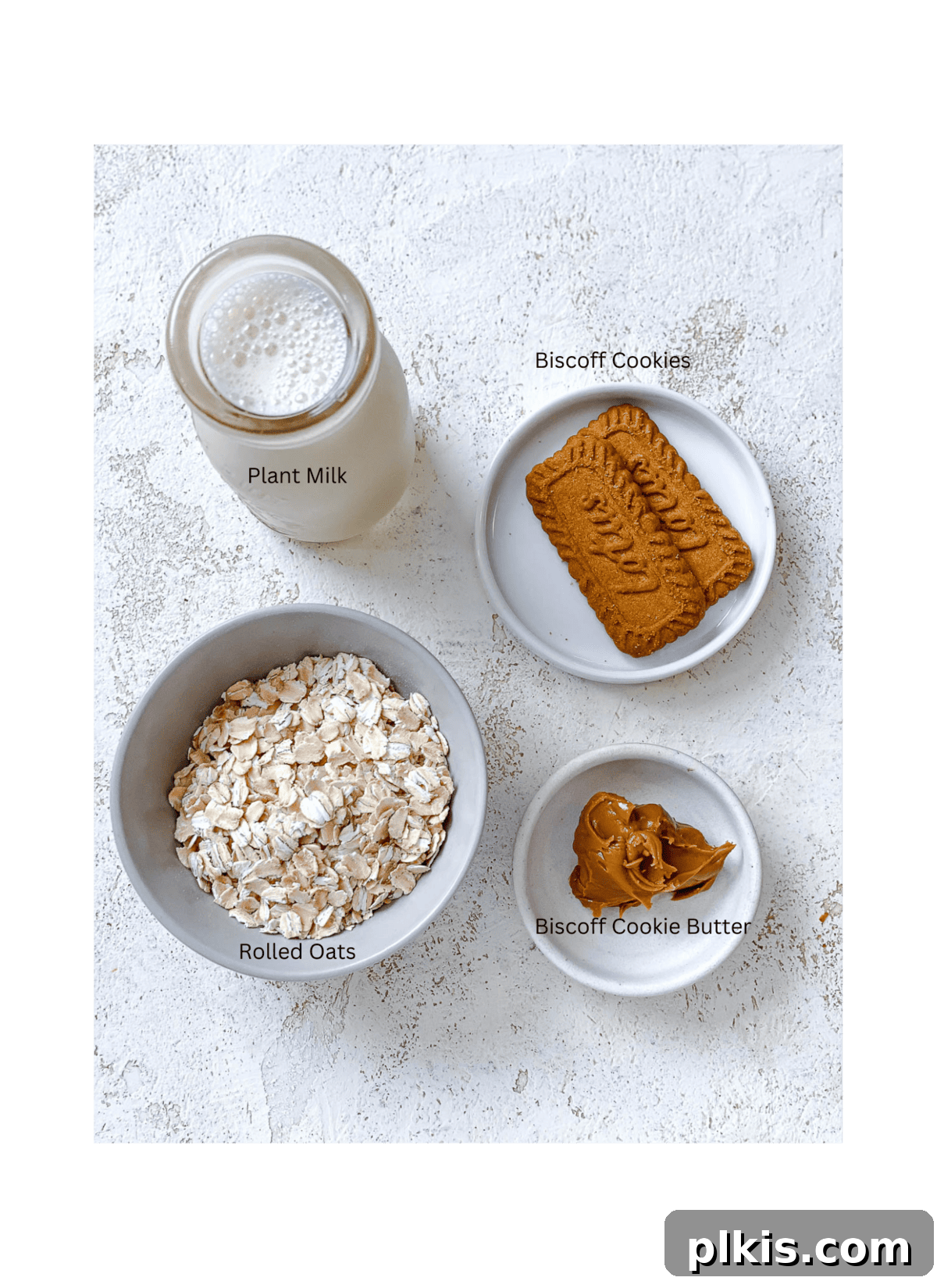 Dreamy Biscoff Overnight Oats 3 Individual ingredients for Biscoff Overnight Oats, including rolled oats, plant-based milk, Biscoff cookie butter, and whole Biscoff cookies, laid out on a clean surface.