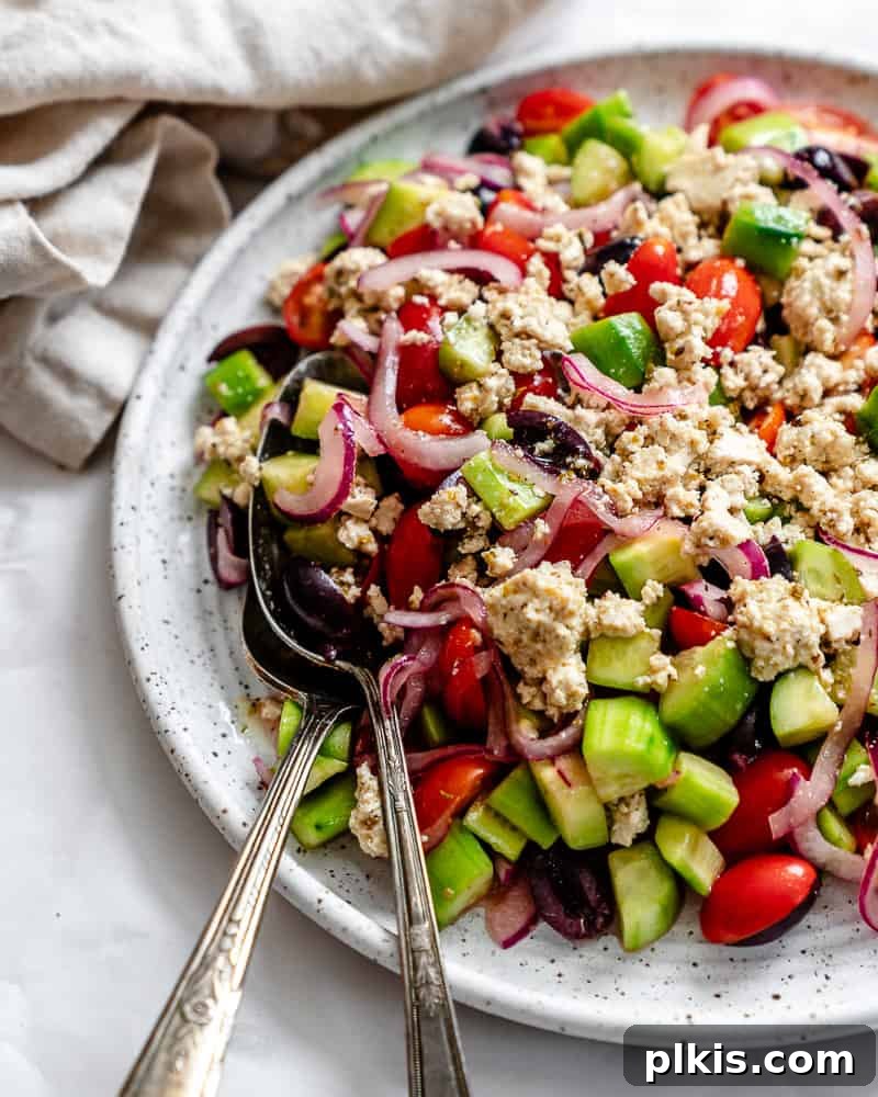 A beautifully plated Greek Cucumber Salad, showcasing fresh, vibrant ingredients like diced cucumbers, halved cherry tomatoes, black olives, and crumbled vegan feta, all tossed in a zesty vinaigrette.