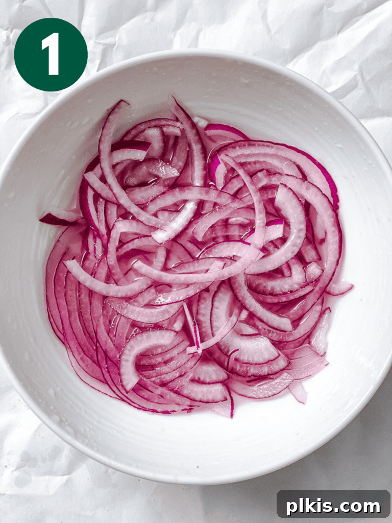 Process shot showing thinly sliced red onions soaking in a bowl with lemon juice and salt, preparing them for the salad.