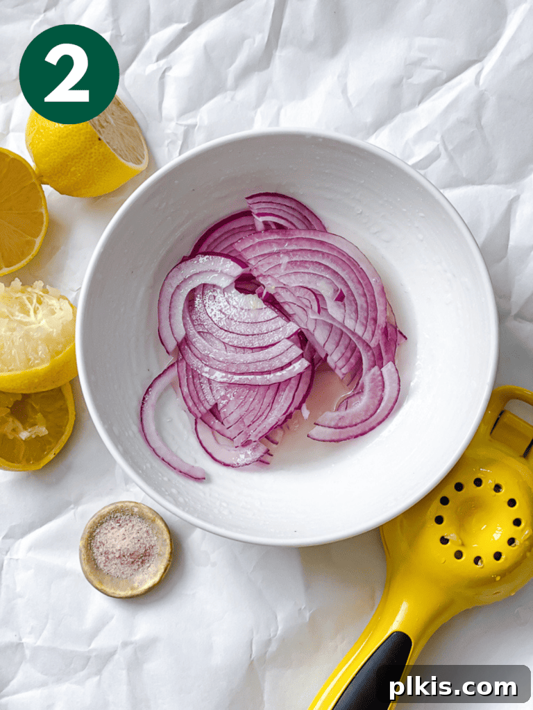 A closer view of the sliced onions in a bowl, with fresh lemons and a salt shaker visible in the soft background, indicating the start of the preparation.