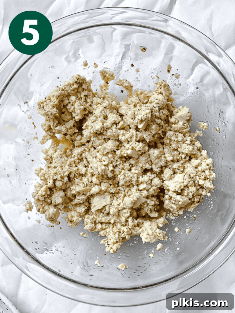 A bowl filled with crumbled tofu generously coated in the aromatic Greek marinade, set aside for flavor infusion.