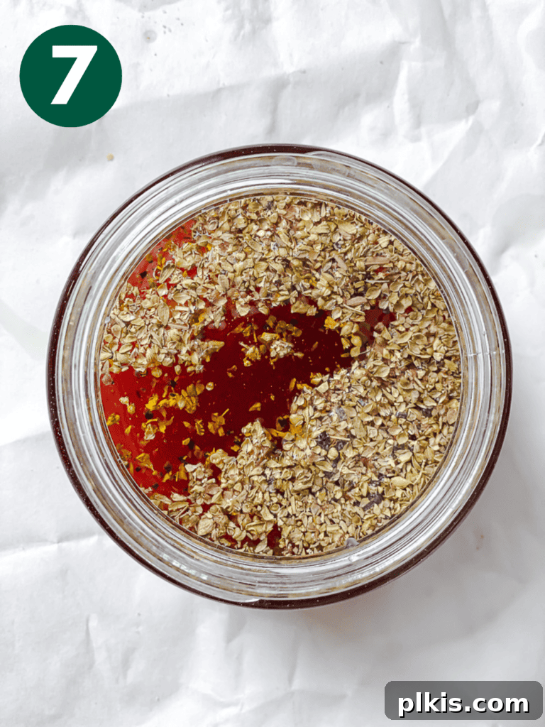 A glass jar with a lid, containing the freshly prepared Greek salad dressing with olive oil, herbs, and spices, ready to be shaken and mixed.