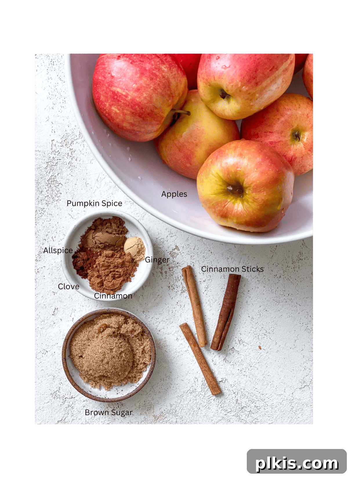 Cozy Spiced Apple Warmer 3 A selection of ingredients for Mulled Apple Cider, including apples, spices, and sweetener, arranged on a white surface.