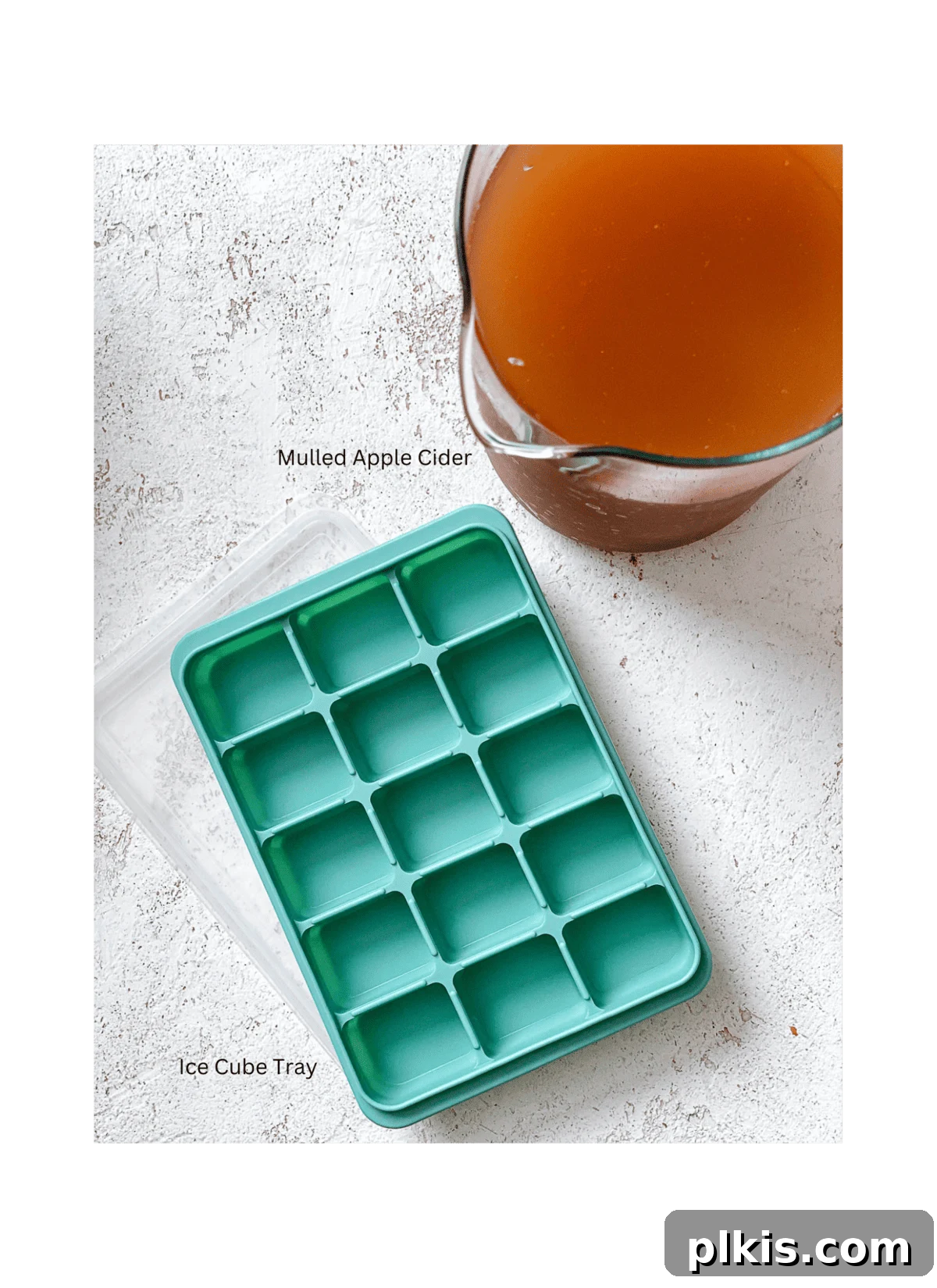 Frozen Apple Cider Delight 3 A collection of ingredients for an Apple Cider Slushie, including bottles of apple cider, spices, and an ice cube tray, laid out on a clean white surface.