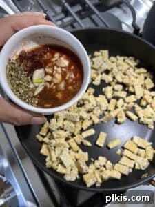 process of adding flavoring sauce to tempeh on a black griddle, mixing thoroughly