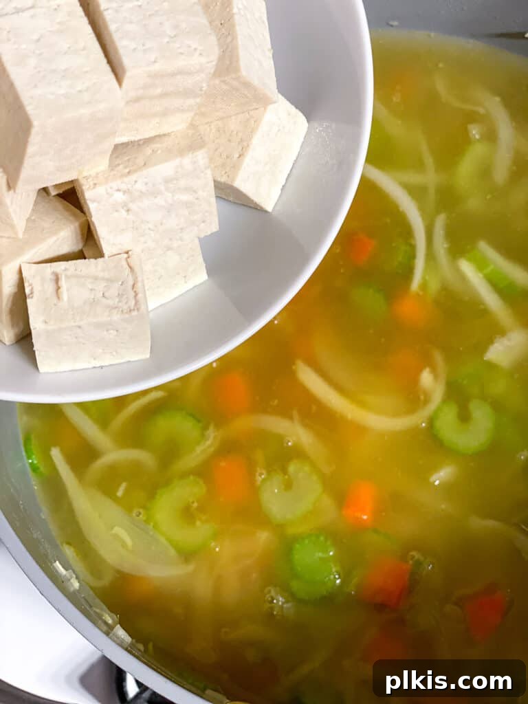 Vegan Chicken Noodle Soup: Stovetop, Instant Pot, and Slow Cooker 9 process shot of adding tofu to soup