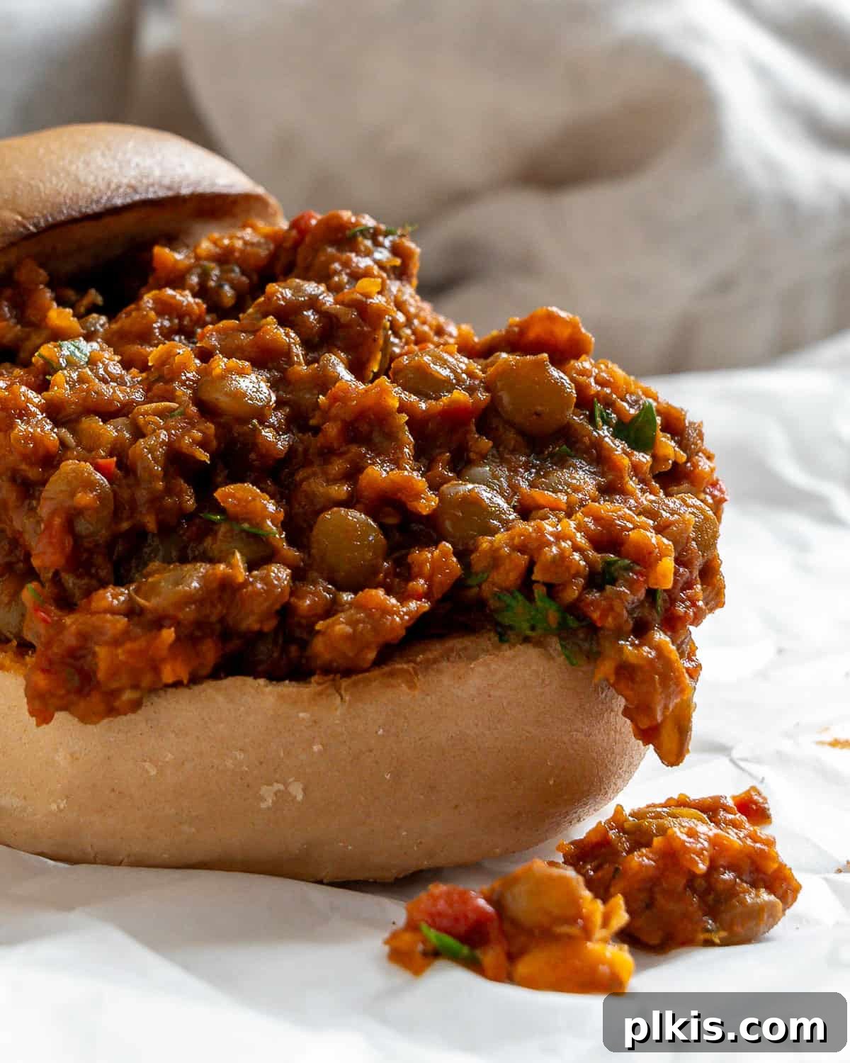 Hearty Lentil Sloppy Joes for Stove Top or Slow Cooker 19 A close-up of a delicious Lentil Sloppy Joe served in a hamburger bun, garnished with fresh parsley.