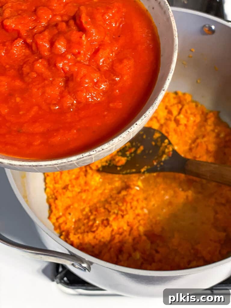 Hearty Lentil Sloppy Joes for Stove Top or Slow Cooker 10 Process shot of adding tomato sauce to the sautéed vegetables in a pan.