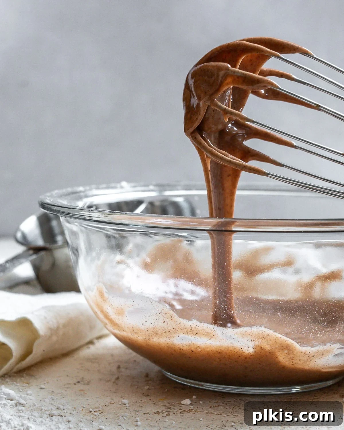 Golden Pumpkin Spice Glaze 2 A glass bowl filled with rich, creamy pumpkin spice glaze, with a whisk drizzling the glaze, showcasing its perfect consistency. Ideal for topping fall baked goods.
