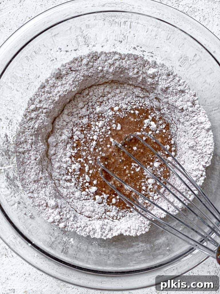 Golden Pumpkin Spice Glaze 4 A close-up process shot showing powdered sugar, pumpkin spice, and plant-based milk being whisked together in a clear glass bowl, illustrating the initial mixing stage of the glaze.
