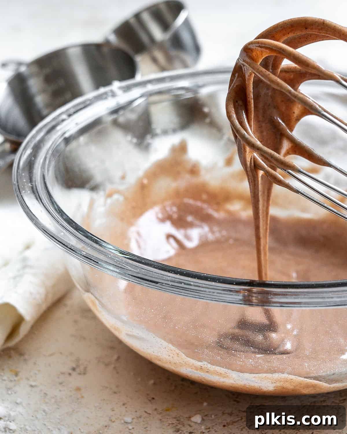 Golden Pumpkin Spice Glaze 5 A whisk lifting a rich, consistent stream of homemade Pumpkin Spice Glaze from a glass bowl, ready to adorn your favorite autumn desserts.