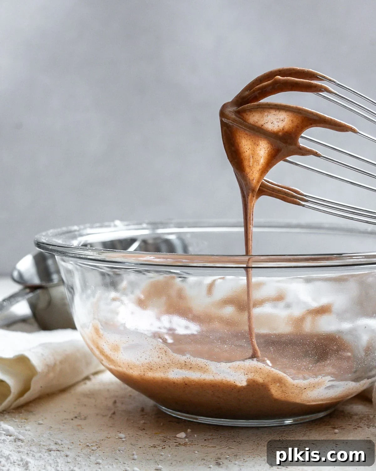 Golden Pumpkin Spice Glaze 6 The perfect consistency of homemade Pumpkin Spice Glaze being expertly drizzled from a whisk into a clear glass bowl, showcasing its readiness for fall desserts.
