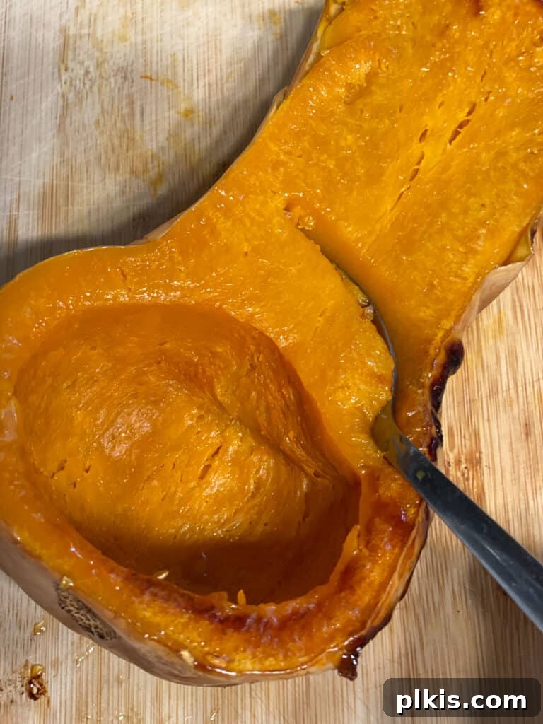 Golden Thai Squash Elixir 8 A spoon scooping the soft, roasted flesh from a butternut squash half into a bowl.