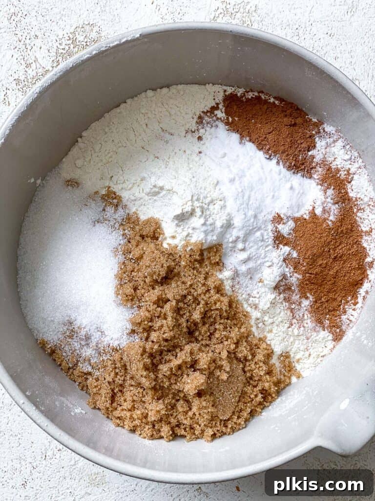 Dry ingredients for Vegan Pumpkin Bundt Cake, including flour, sugars, and spices, added to a large mixing bowl.