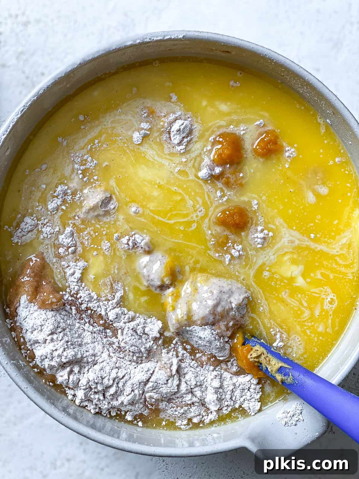 Wet ingredients for Vegan Pumpkin Bundt Cake, including plant-based milk, melted vegan butter, and pumpkin puree, added into a well in the dry ingredients.