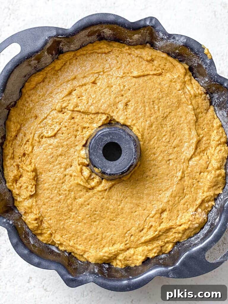 Vegan Pumpkin Bundt Cake batter poured into a prepared bundt pan, smoothed evenly with a spatula, ready for baking.