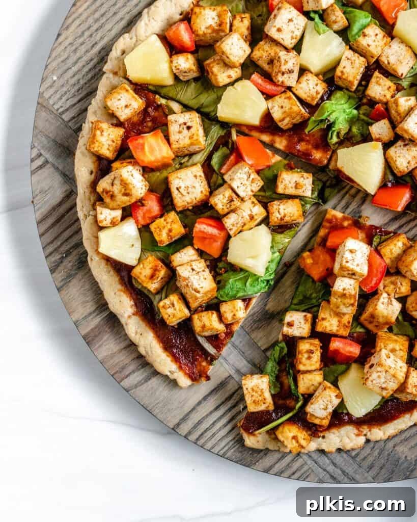 Plant-Powered BBQ Pizza 2 A completed vegan BBQ pizza, expertly sliced into quarters, resting on a textured circular wooden board. The pizza, garnished with vibrant toppings, is presented against a clean white background, highlighting its delicious appeal.