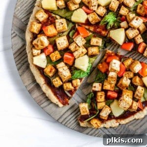 Plant-Powered BBQ Pizza 10 completed vegan bbq pizza sliced into quarters on a textured circular board against a white background