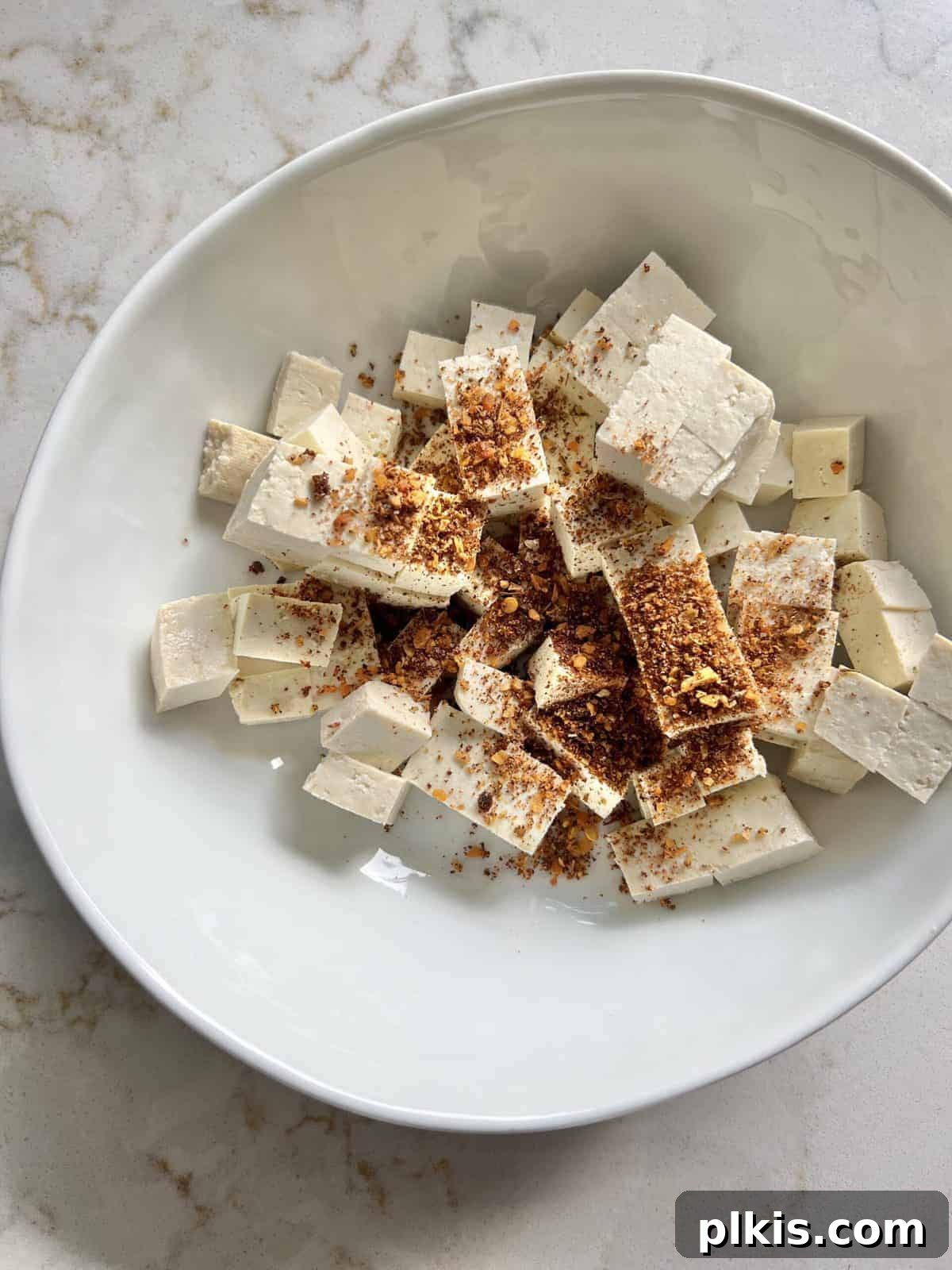 Plant-Powered BBQ Pizza 6 Diced tofu in a white bowl, with a generous sprinkle of Cajun seasoning being added, illustrating the flavoring process.