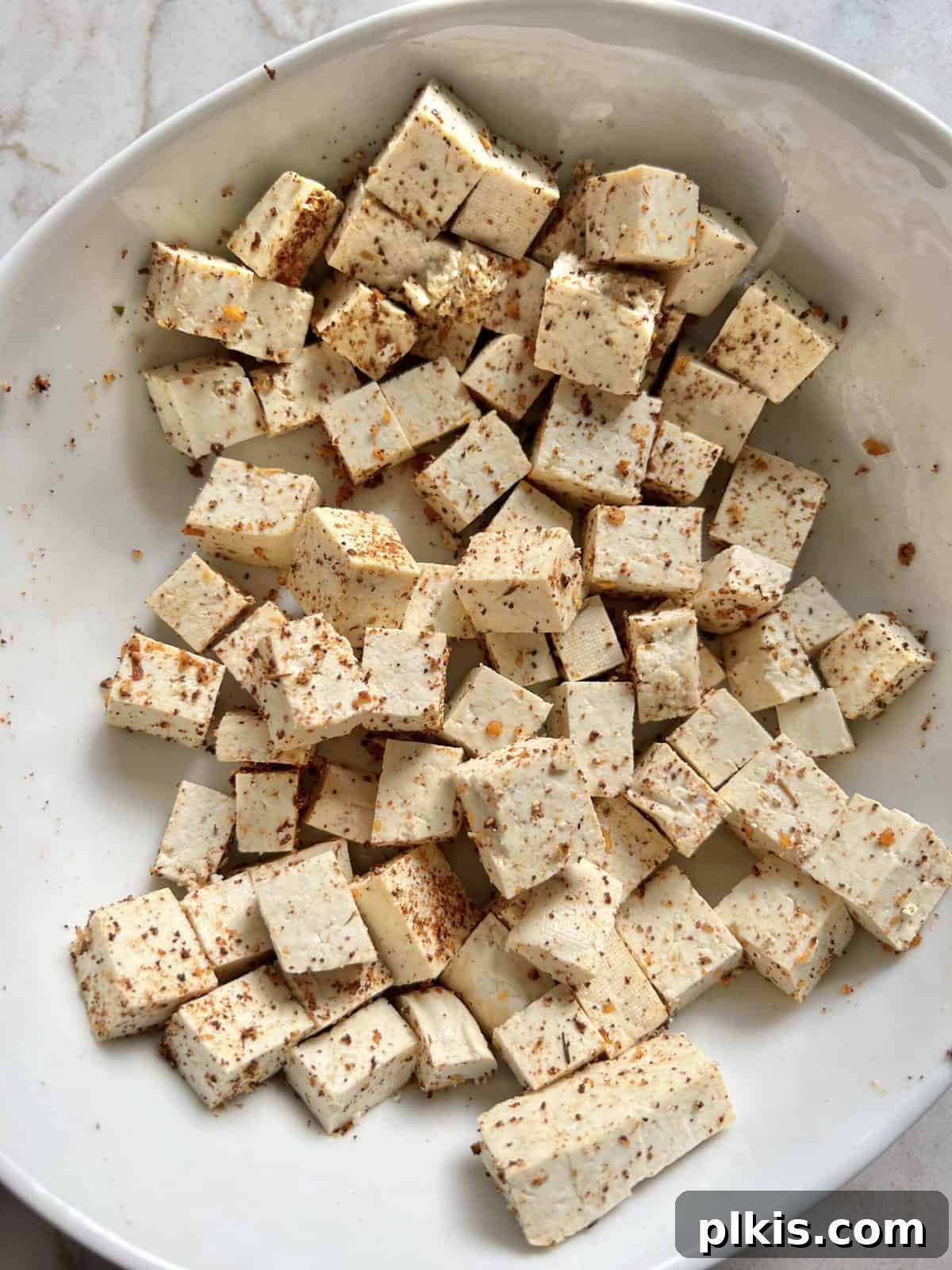 Plant-Powered BBQ Pizza 7 A white bowl contains diced tofu mixed thoroughly with spices, showing the tofu absorbing the flavors before cooking.