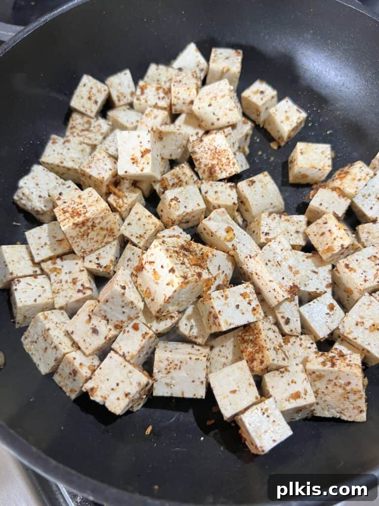 Plant-Powered BBQ Pizza 8 Close-up view of seasoned tofu cooking in a black non-stick pan, sizzling and browning on the stovetop, indicating the pan-frying process.