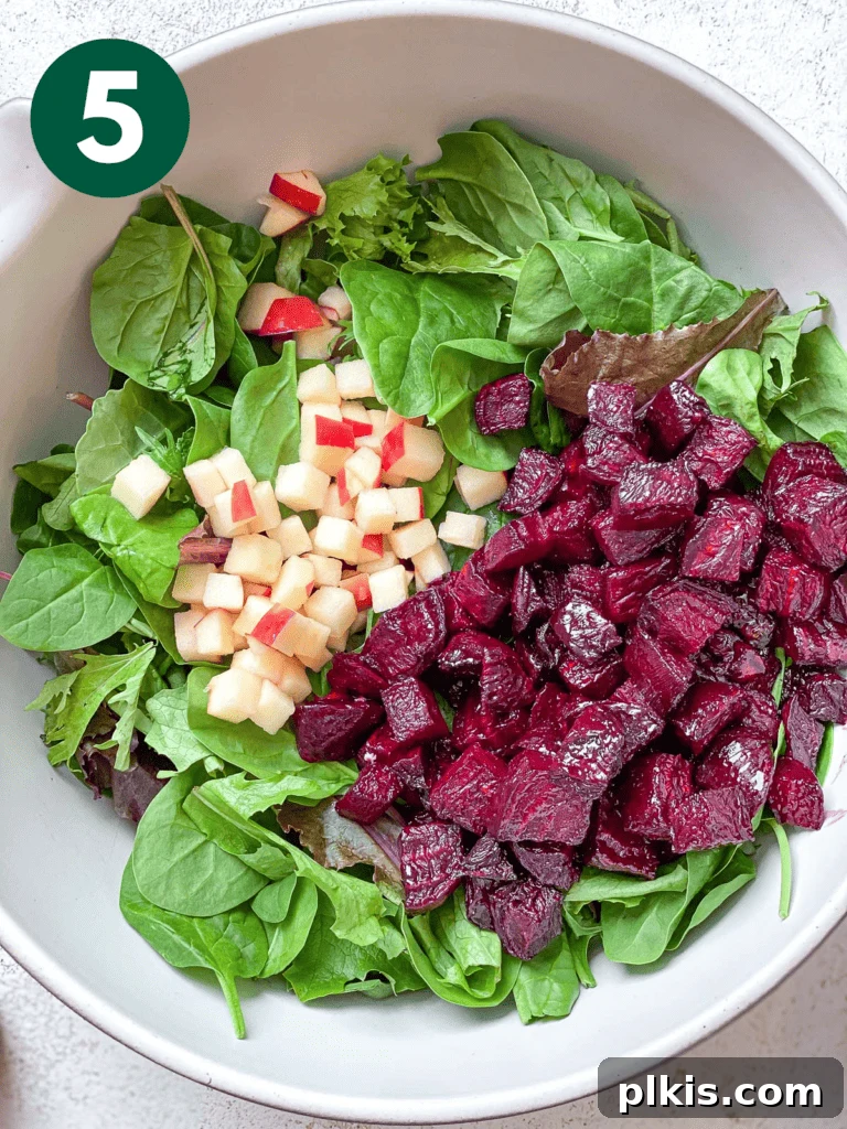 Vibrant Roasted Beet Salad with Vegan Feta and Crisp Apple 9 Process shot of adding leafy greens, diced apple, and roasted beets to a salad bowl.