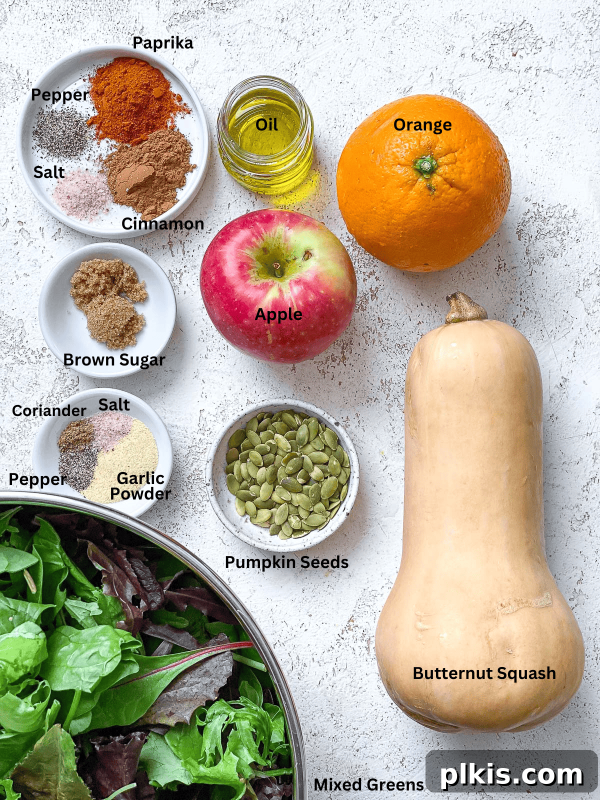 A collection of fresh ingredients for Easy Butternut Squash Salad laid out on a white surface, including squash, apples, and spices.