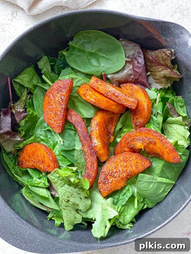 Process shot of assembling the Easy Butternut Squash Salad, combining greens with roasted squash and apples in a large bowl.