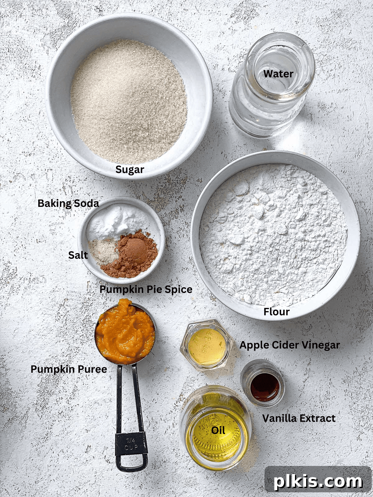 Spiced Vegan Pumpkin Bites 3 Ingredients for Vegan Pumpkin Cupcakes laid out on a white surface, including pumpkin puree, flour, sugar, oil, and spices.