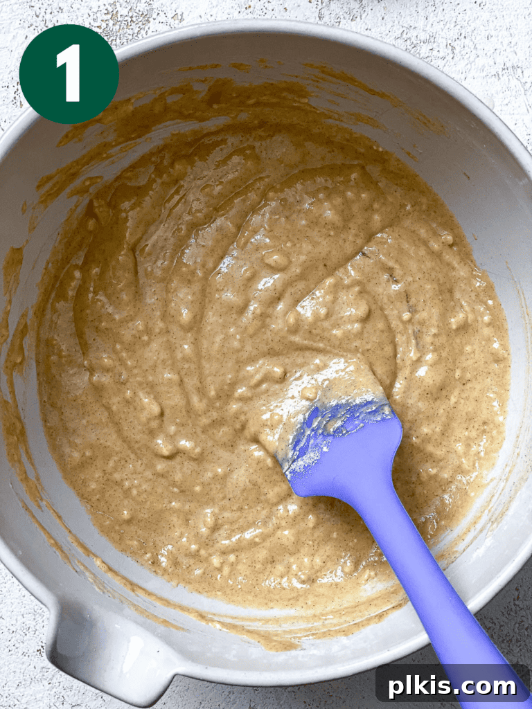 Spiced Vegan Pumpkin Bites 4 Process shot of mixing ingredients for vegan pumpkin cupcakes in a large bowl with a spatula, showing a smooth, thick batter.