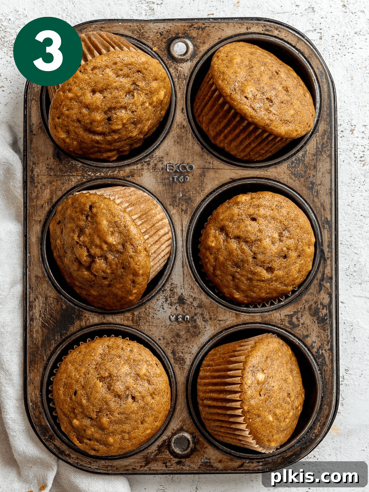 Spiced Vegan Pumpkin Bites 6 Freshly baked Vegan Pumpkin Cupcakes cooling in a baking tin, against a clean white surface.
