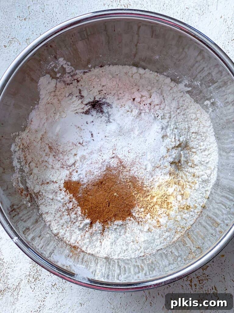 Cozy Vegan Gingerbread Spice Cake 6 A process shot showing dry ingredients being carefully added to the wet batter in a mixing bowl.