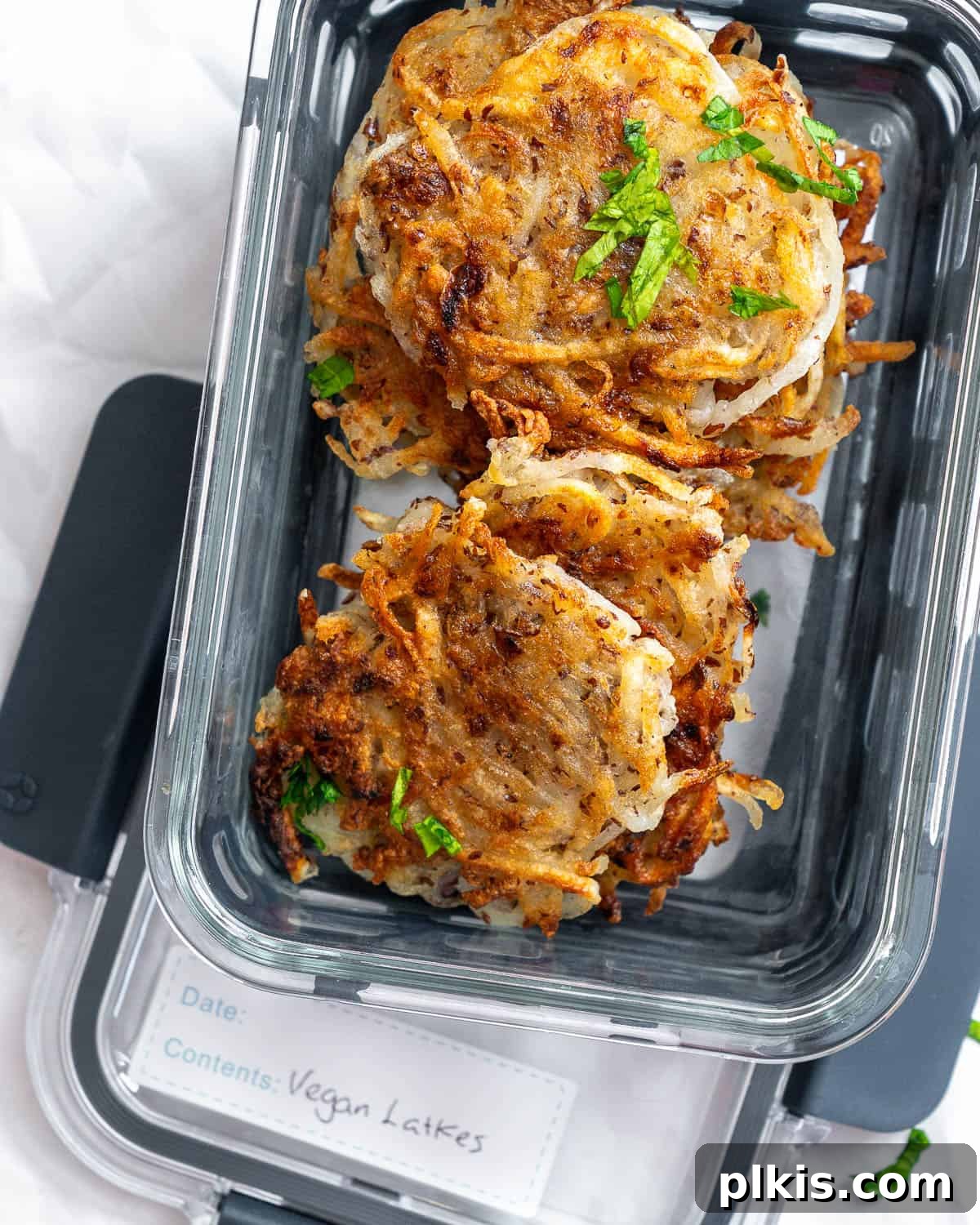Crispy Vegan Potato Latkes 11 A container filled with cooled, completed Vegan Potato Latkes, neatly stacked and ready for storage or meal prep.
