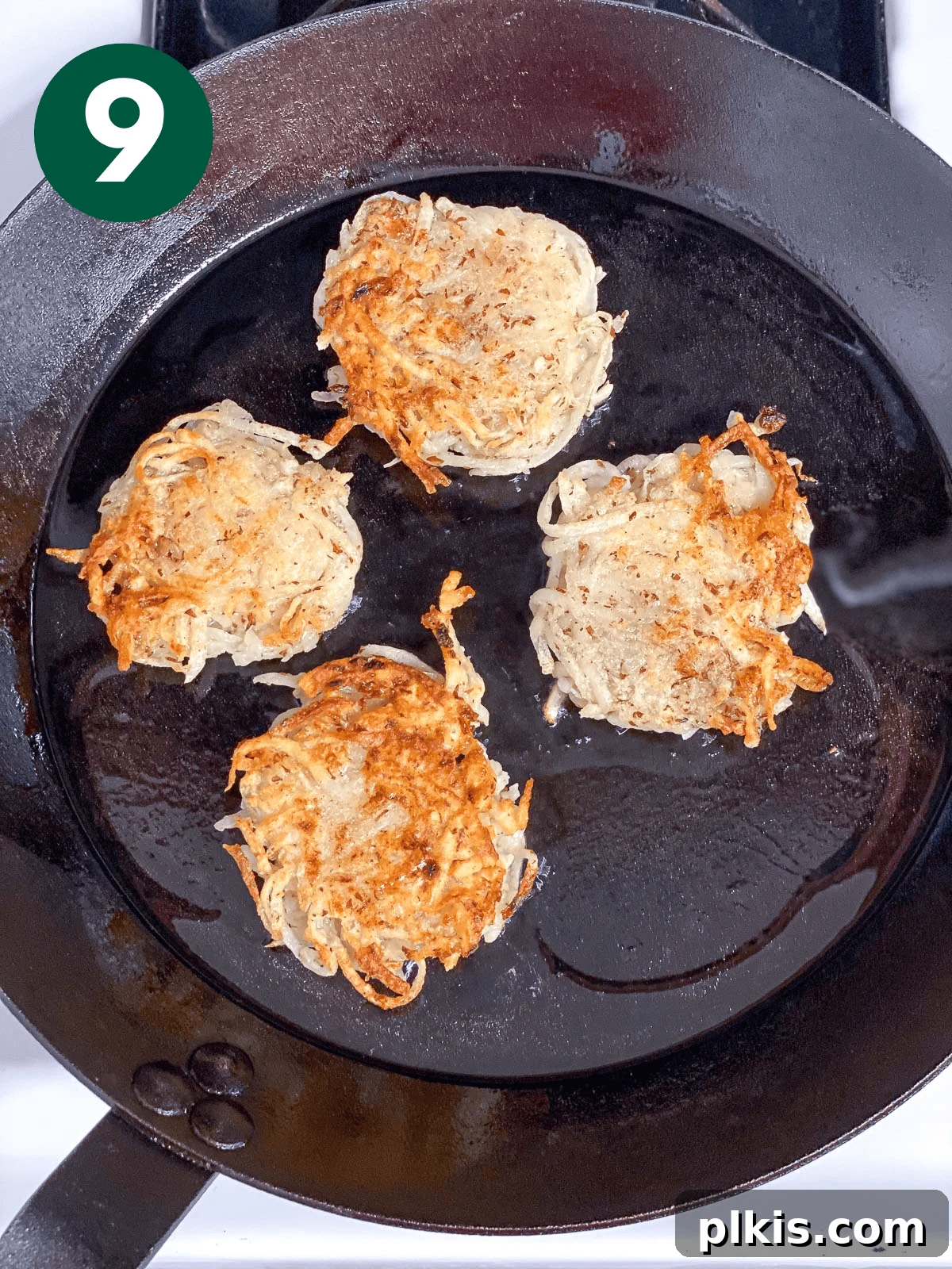 Crispy Vegan Potato Latkes 9 Process shot of several vegan potato latkes sizzling and browning in a hot skillet filled with oil, demonstrating the frying stage.