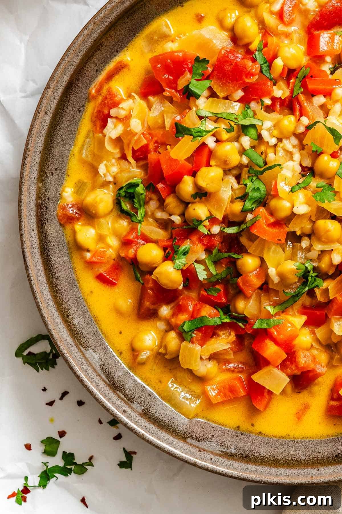 A vibrant bowl of creamy Coconut Chickpea Curry Soup, garnished with fresh cilantro, ready to be enjoyed. The rich orange hue of the soup highlights its warmth and inviting nature, perfect for a cozy meal.