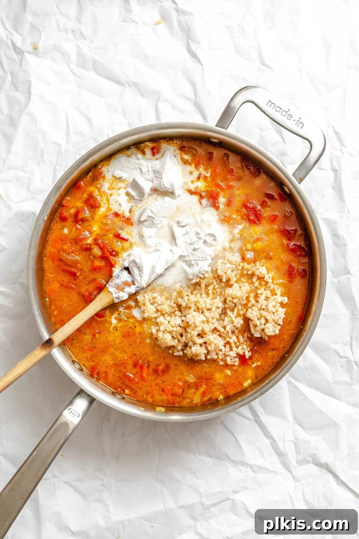 Process shot showing creamy coconut milk and cooked brown rice being stirred into the simmering curry soup, enriching its texture and flavor.