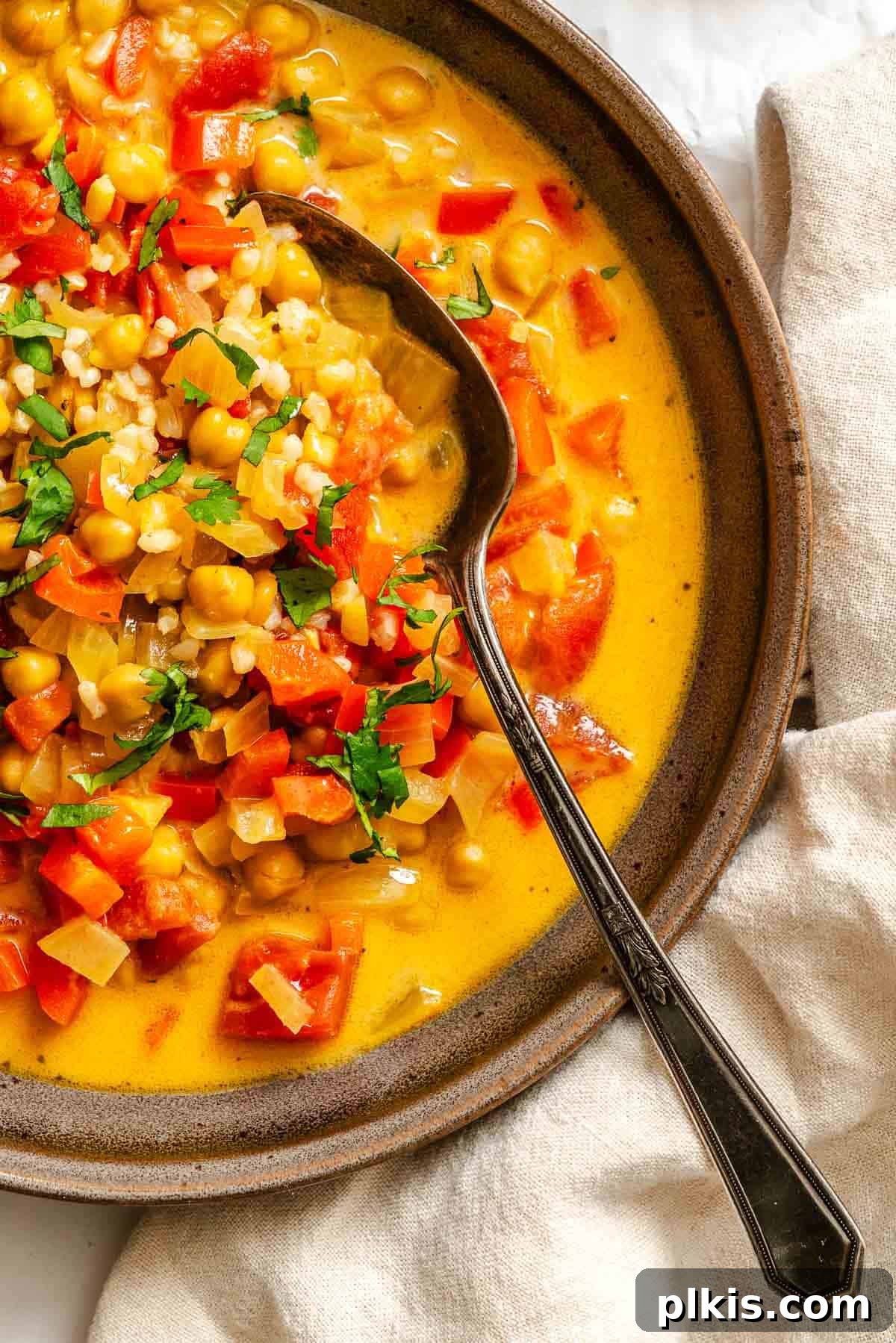 A large pot filled with the finished Coconut Chickpea Curry Soup on a white surface, showcasing its appealing color and consistency, ready for serving.
