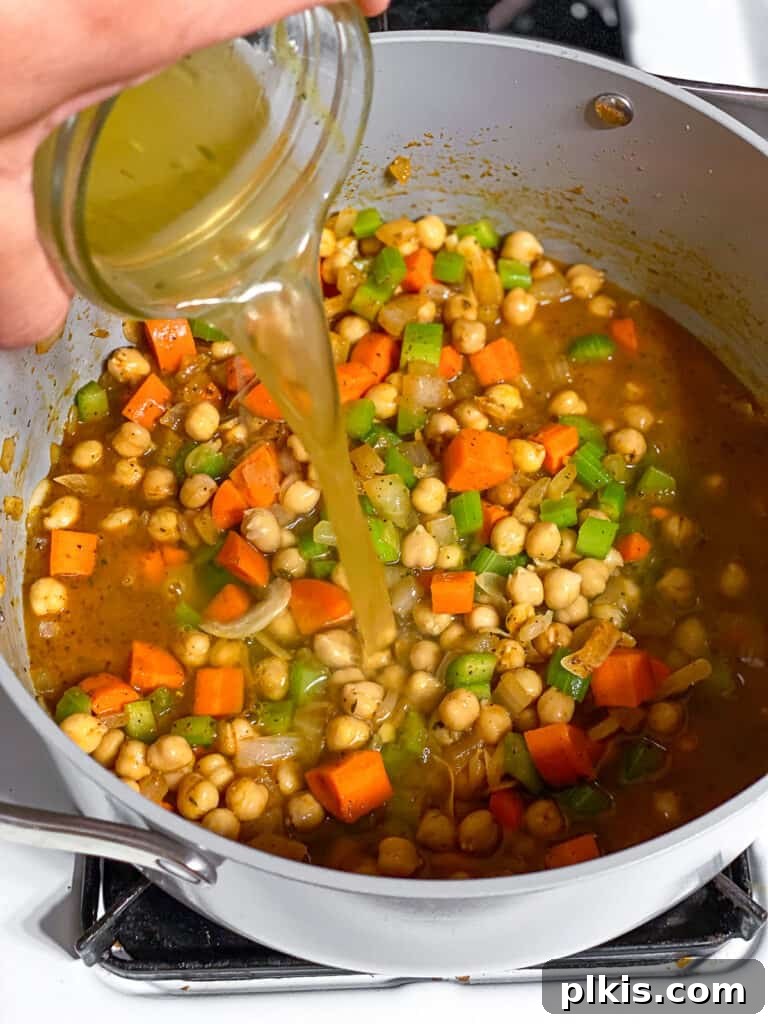 Comforting Vegan Chickpea Noodle Soup 5 Process shot illustrating vegetable broth being poured into a pot with sautéed vegetables and chickpeas.